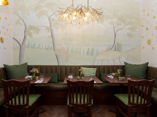 Green banquettes beneath the hand-painted mural and brass chandelier